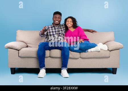 Glückliches junges afroamerikanisches Paar schaut zusammen im Wohnzimmer fern, entspannt zu Hause Stockfoto