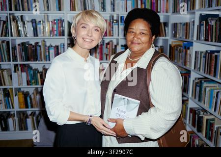 Porträt einer kaukasischen Frau mittleren Alters und einer afroamerikanischen Frau mittleren Alters, die in einer Bibliothek stehen, ein Buch halten und lächeln. Nützlich für Bildung, Alphabetisierung, Gemeinschaftsaufklärungskampagnen Stockfoto