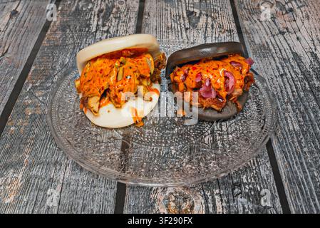 Weiße und schwarze Bao Buns gefüllt mit Fleisch und scharfer Soße auf einem Glas Teller Stockfoto