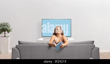 Mädchen auf einem Sofa, das ein offenes Buch hält, isoliert auf weißem Hintergrund Stockfoto