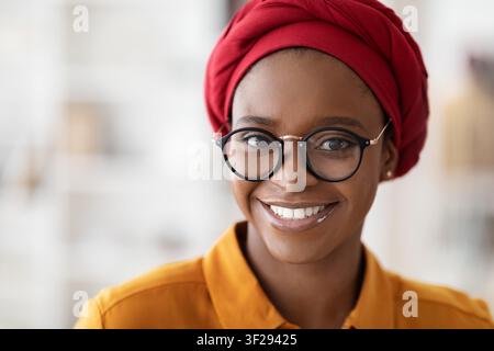 Lächelnde schwarze Frau mit rotem Kopftuch und Brille, Inneneinrichtung, Porträt Stockfoto