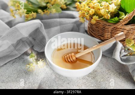 Natürlicher Lindenhonig in einer weißen Schüssel mit einem hölzernen Löffel, umgeben von frischen Blumen Stockfoto