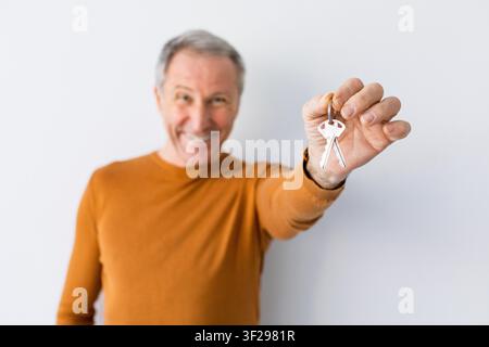 Zufriedener Senior mit weißer Haut, der mit einem Lächeln Schlüssel hält, Heimsetting, Immobilienkonzept Stockfoto