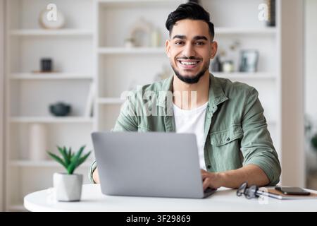 Lächelnder junger südasiatischer Mann arbeitet an einem Laptop im Home Office, Business-Konzept Stockfoto