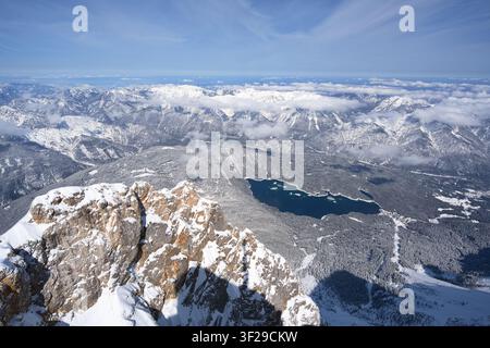 Eine hochwinklige Luftpanoramaaufnahme des tiefblauen Eibsees mit seinen kleinen Inseln, vollständig umgeben von einem dichten, schneebedeckten Kiefernwald in Stockfoto