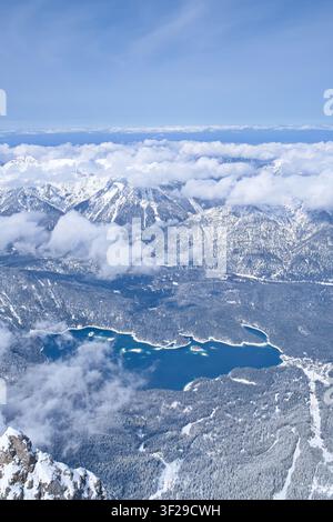 Eine hochgelegene, vertikale Landschaftsaufnahme vom Gipfel der Zugspitze aus, die den türkisfarbenen Eibsee zeigt, umgeben von schneebedeckten Kiefern Stockfoto