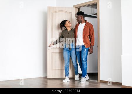 Glückliches schwarzes Paar betritt gemeinsam das neue Zuhause, lächelt und umarmt sich Stockfoto