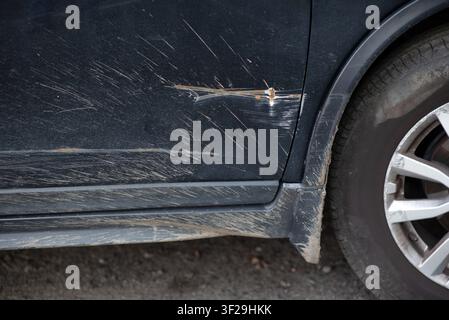 Nahaufnahme eines tiefen Kratzers und einer rostigen Delle an einer schmutzigen schwarzen Autotür. Stockfoto