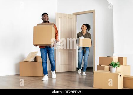Glückliches junges afroamerikanisches Paar trägt Kisten und zieht in ein neues Zuhause ein, aufgeregt und fröhlich Stockfoto