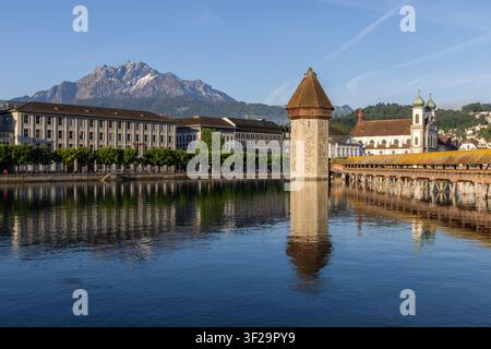 Blick auf die historische Kapellbrücke und den Wasserturm, die sich im Fluss Reuss spiegeln, mit dem Pilatus im Hintergrund unter einem klaren blauen Himmel in Luzern Stockfoto