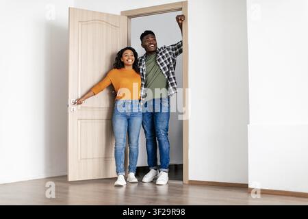 Glückliches Paar afrikanisch-amerikanischer junger Erwachsener, die an einer offenen Tür stehen und lächeln Stockfoto