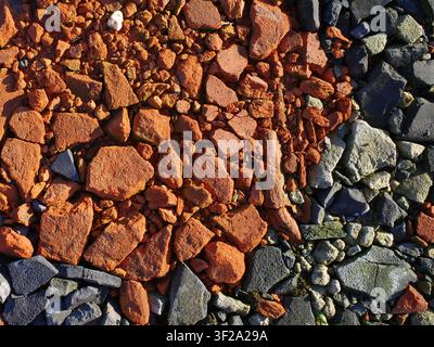 Eine Oberfläche, die aus zwei verschiedenen Arten von zerkleinerten Dachziegeln besteht, rot und grau. Sie besteht aus unregelmäßig geformten, gezackten Stücken mit einer rauen Textur. Stockfoto