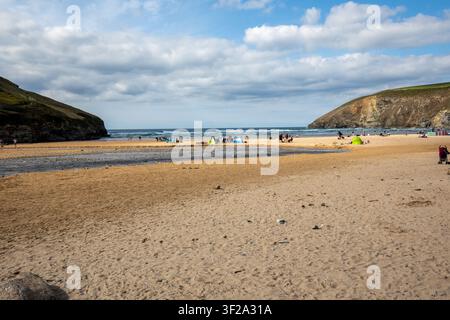 Urlauber entspannen sich auf dem breiten goldenen Sandstrand von Mawgan Porth Beach bei Ebbe, eingerahmt von Klippen an der Nordküste Cornwalls, England, UK. Stockfoto