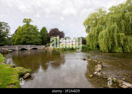 Die historische Stein-Sheepwash-Brücke und ein traditionelles Cottage neben den klaren Gewässern des Flusses Wye in Ashford in the Water, Derbyshire, UK. Stockfoto