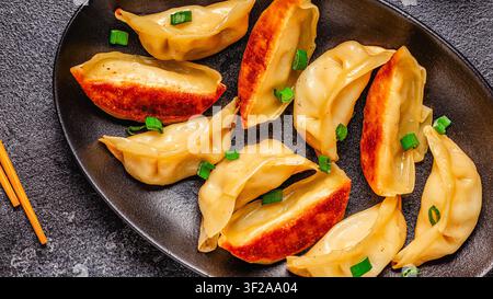 Knödel werden auf einem schwarzen Teller mit grüner Zieronion garniert in einer Kücheneinrichtung serviert Stockfoto