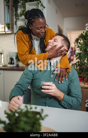 Liebevolles interrassisches Paar, das sich in moderner Küche zu Hause umschließt Stockfoto