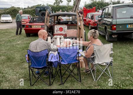 Paar entspannt in Klappstühlen sitzend und ein Picknick im Freien auf einem Oldtimertreffen genießend. England UK Stockfoto