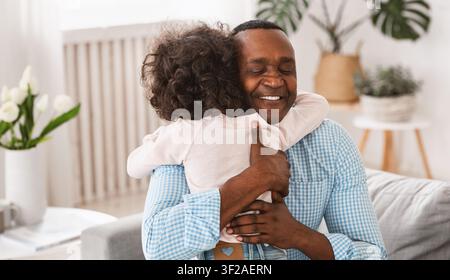 Großeltern Enkelkind Beziehung. Älterer afroamerikanischer Mann umarmt seine Enkelin zu Hause Stockfoto