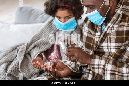 Handhygiene während der Pandemie. Afroamerikanischer Mann und Enkelin mit Masken, die zu Hause antiseptisch auftragen Stockfoto
