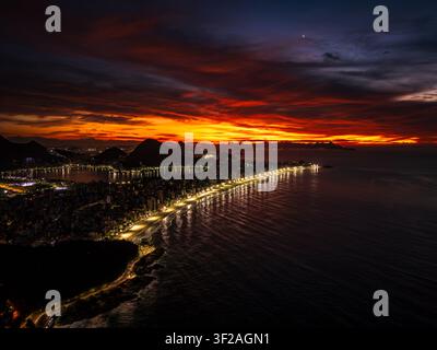 Luftaufnahme der beleuchteten Küste bei Sonnenaufgang mit dramatischen orangefarbenen und lila Wolken über dem Ozean und den Bergen in Rio de Janeiro, Bundesstaat Ri Stockfoto