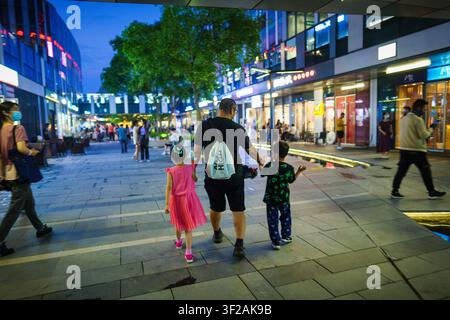 Ein Mann, der Händchen mit zwei Kindern hält, geht nachts auf einer belebten Straße. Stockfoto