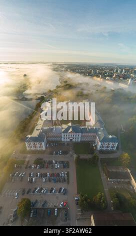 Luftaufnahme des Jelgava-Schlosses, umgeben von Morgennebel, üppigen Bäumen und einem Parkplatz in Jelgava, Lettland. Stockfoto