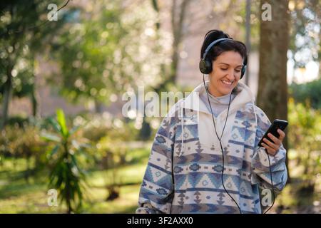 Junge Frau lächelt, genießt Musik mit kabelgebundenen Kopfhörern und Smartphone im Freien Stockfoto