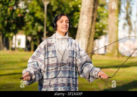 Frau genießt Outdoor-Fitness, hört Musik, während sie sich im Park zum Seilspringen bereitmacht Stockfoto