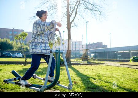 Frau mit Kopfhörern, die an einem sonnigen Tag in einem öffentlichen Park ein Fitness-Workout macht Stockfoto