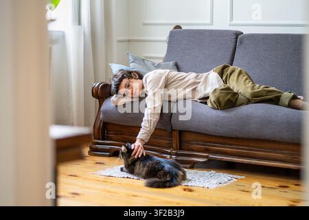 Ruhige, sorglose Frau liegt faul auf der Couch und genießt das friedliche Leben in Gesellschaft einer Hauskatze. Stockfoto