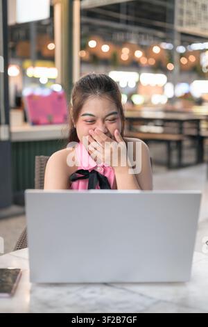 Eine vertikale Mittelaufnahme einer fröhlichen südostasiatischen thailändischen Isan-Frau, die sich mit der Hand über den Mund bedeckt und kichert, während sie auf ihr silbernes La hinunterschaut Stockfoto