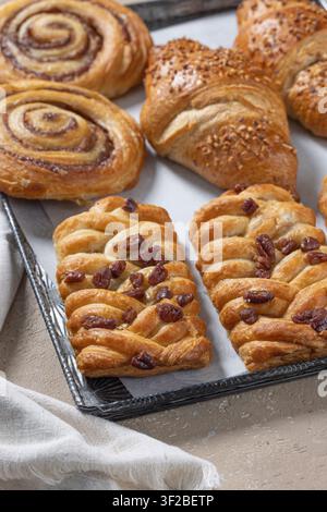 Verschiedene frisch gebackene süße Brötchen auf einer rustikalen Pfanne auf einem beigen Küchentisch. Hausgemachte Gebäckstücke mit goldener Kruste in einer gemütlichen Bäckerei-Umgebung, perfekt für Brea Stockfoto