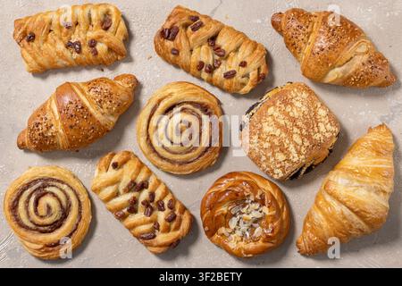 Oberansicht einer Auswahl frisch gebackener süßer Brötchen, die auf einem beigen Hintergrund angeordnet sind. Minimale Bäckereikomposition mit goldenen hausgemachten Gebäckstücken wi Stockfoto