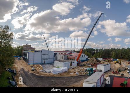 Luftbild einer Baustelle mit modularen Gebäudestrukturen, großen Kränen und schwerer Bautechnik unter einem bewölkten Himmel in Lettland. Stockfoto