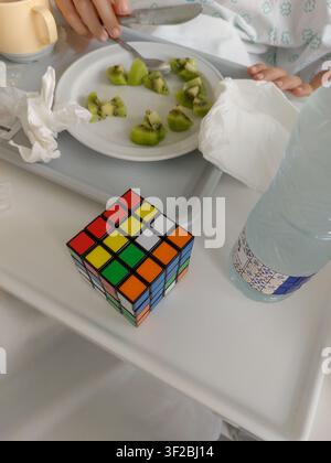Hohe Winkel, Nahaufnahme auf einen farbenfrohen 4x4-Rubik-Würfel auf einem Krankenhaus-Bett-Essteller. Im Hintergrund, teilweise unscharf, sind die Hände eines Kindes Stockfoto