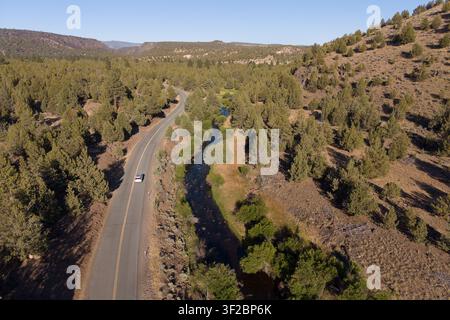 Drohnenluftbild eines Autos auf der Jess Valley Road entlang des Pit River im Modoc County, Kalifornien, durch Wacholderwald. Stockfoto