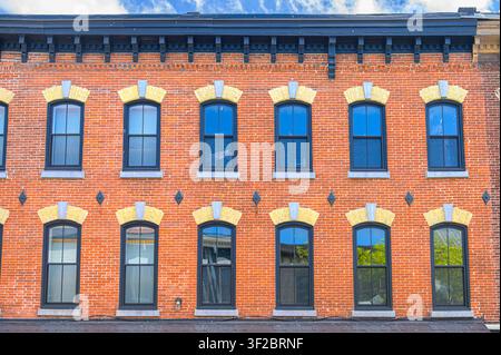 Historische rote Backsteinfassade eines Gewerbegebäudes mit gewölbten Fenstern und dekorativer Mauerarbeit. Stockfoto