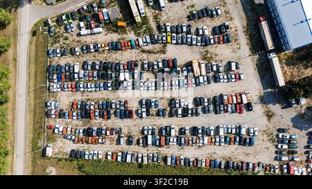 Luftaufnahme eines großen Freiluft-Autoverwerterhofs, gefüllt mit zahlreichen geparkten Fahrzeugen, Lastwagen und Anhängern, die in Reihen auf einem Schotterplatz in Vojvodi angeordnet sind Stockfoto