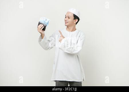 muslimischer Mann hält Rupiah-Geldnoten in der Brieftasche und macht eine Zeigefingergeste. Menschen religiöses Islam-Lebensstilkonzept. Feier Ramadan Stockfoto