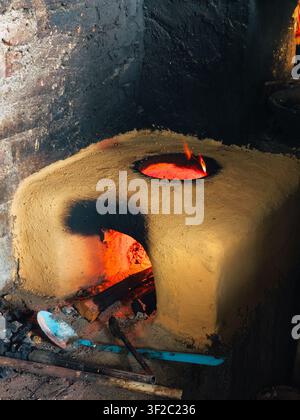 Erdofen glüht vor feuriger Wärme. Offenes Feuer knistert in der grob behauenen Kammer. Werkzeuge liegen neben dem Ofen, bereit für den Einsatz. Staub und Rauch wirbeln umher Stockfoto