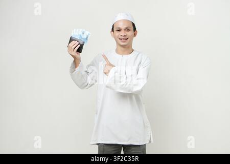 muslimischer Mann hält Rupiah-Geldnoten in der Brieftasche und macht eine Zeigefingergeste. Menschen religiöses Islam-Lebensstilkonzept. Feier Ramadan Stockfoto