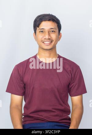 Porträt eines freundlichen jungen asiatischen Mannes in einem lässigen lilafarbenen Hemd, der gegen einen Studiohintergrund warm lächelt. Stockfoto