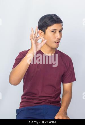 Seitenansicht-Porträt eines freundlichen indonesischen Mannes, der ein lässiges lilafarbenes Hemd trägt und im Studio lächelt. Stockfoto