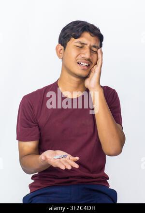 Gestresster junger asiatischer Mann, der auf einen leeren Geldbeutel schaut und seinen Kopf vor Frustration in den Händen hält, isoliert auf weißem Hintergrund. Stockfoto
