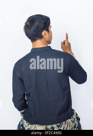 Rückansicht-Porträt eines asiatischen Mannes, der ein traditionelles Batik-Fusionshemd trägt, isoliert auf blauem Hintergrund. Stockfoto