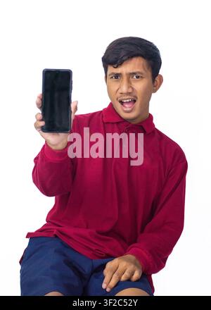 Junger asiatischer Mann trägt ein rotes traditionelles Hemd und hält ein Smartphone mit leerem Bildschirm, der ein Mockup auf weißem Hintergrund zeigt. Stockfoto