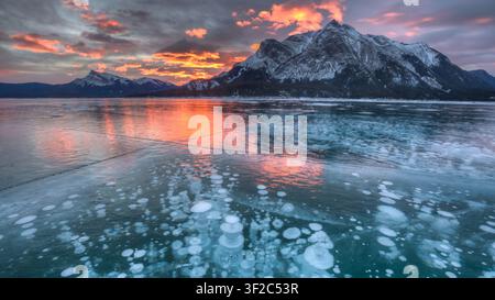 Luftaufnahme von Abraham Lake mit gefrorenen Methanblasen im Eis und schneebedeckten Bergen unter einem lebendigen Sonnenuntergangshimmel in Clearwater County, Al Stockfoto