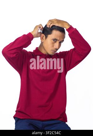 Porträt eines stilvollen asiatischen Mannes in rotem traditionellem Hemd und flacher Kappe, der lässig auf weißem Hintergrund posiert. Stockfoto