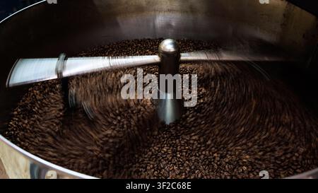 Eine Nahaufnahme einer industriellen Röstmaschine mit einem rotierenden Metallarm, der frisch geröstete Kaffeebohnen in einem professionellen Laden kühlt. Stockfoto