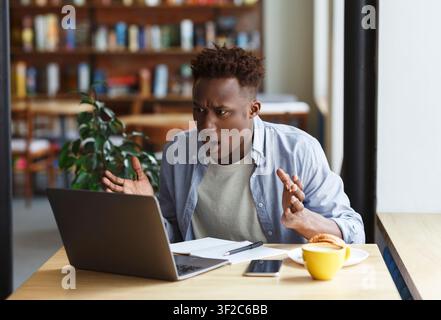 Frustrierter afroamerikanischer Mann mit Laptop, der im Café studiert oder arbeitet Stockfoto